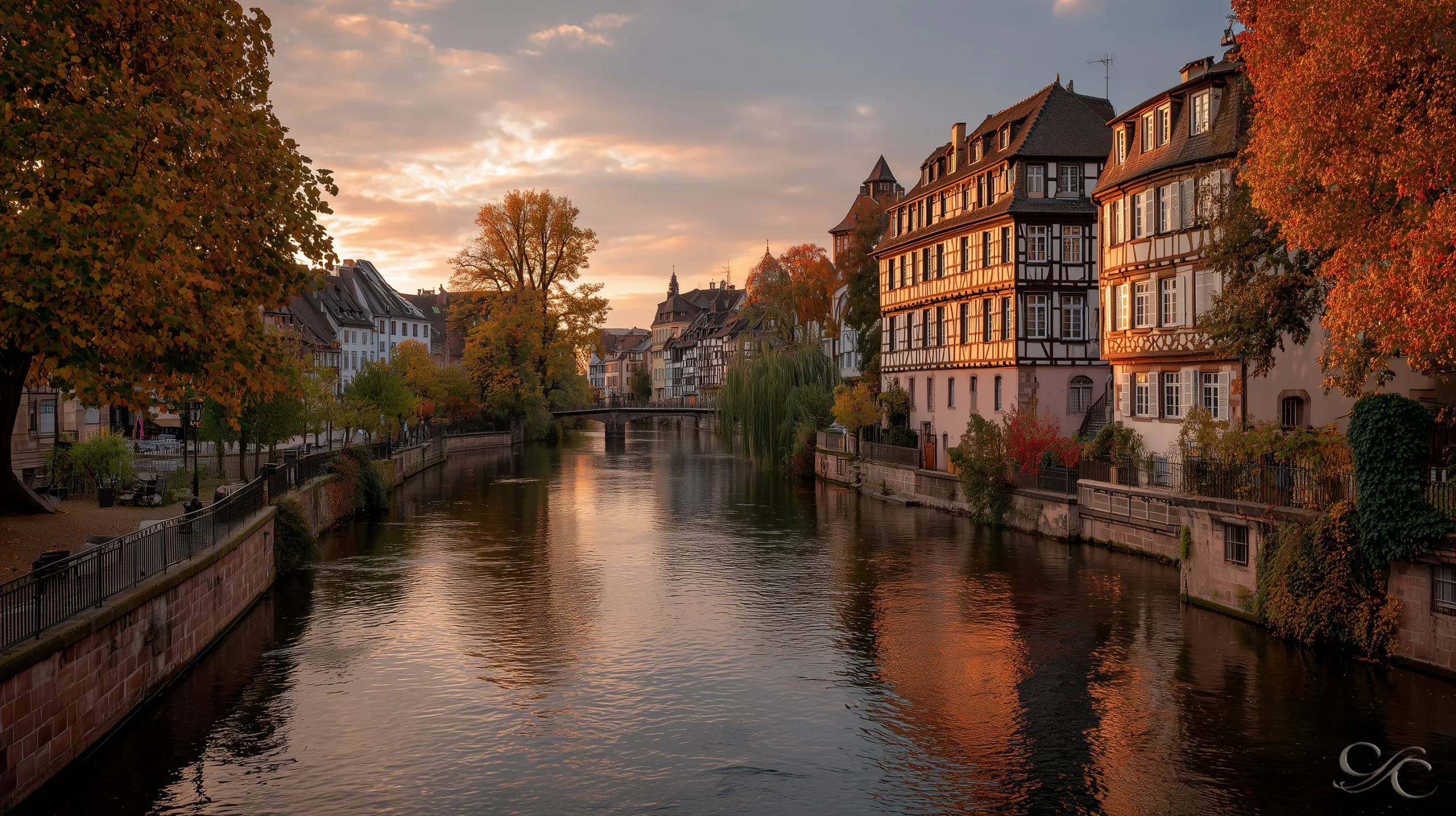 A serene canal flows between historic buildings and autumn trees under a warm sunset sky.